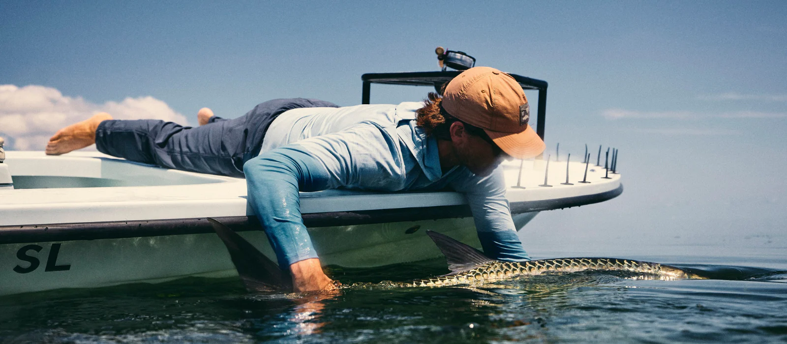 Front Page -Fishing Tackle Sale Man lying at the edge of his boat holding a fish while saltwater fishing